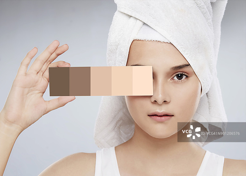 一个女人拿着一张有皮肤颜色的色卡，为她的皮肤选择正确的化妆色调图片素材