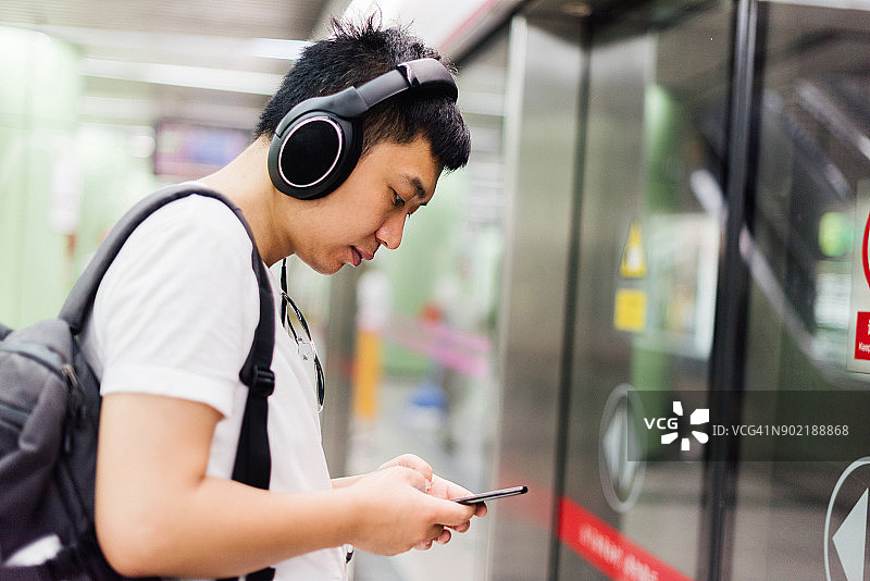 一名年轻人在等地铁的时候一边用智能手机一边听音乐图片素材