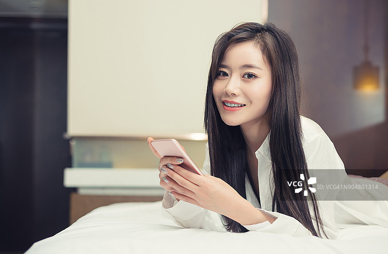 微笑的女人在床上拿着智能手机图片素材