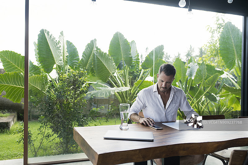 成熟的男人坐在餐桌前郁郁葱葱的花园，写作图片素材