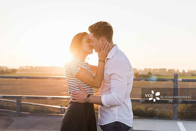 日落时分，一对年轻的情侣在停车场上接吻图片素材
