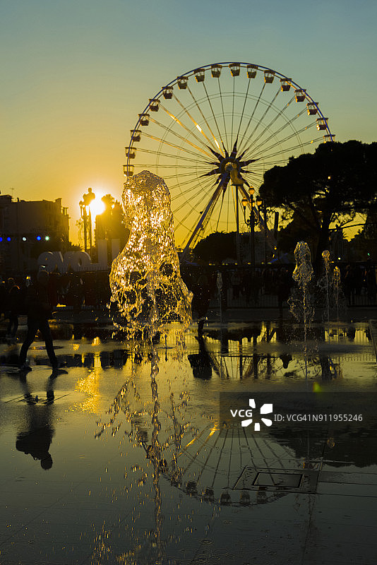 喷泉和摩天轮在日落倒映水，马塞纳广场图片素材
