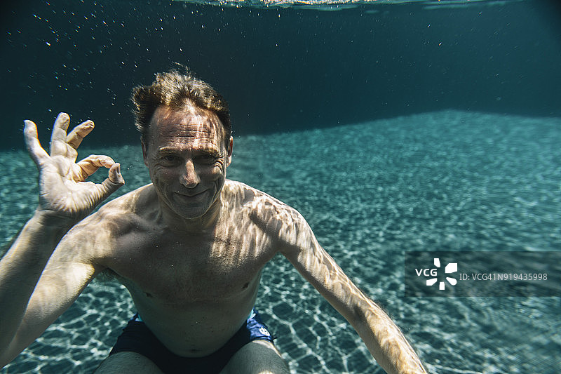 一个微笑的男人在游泳池里做ok手势的肖像图片素材