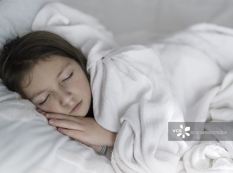 年轻的女孩睡在一张有白色床单的床上。图片素材