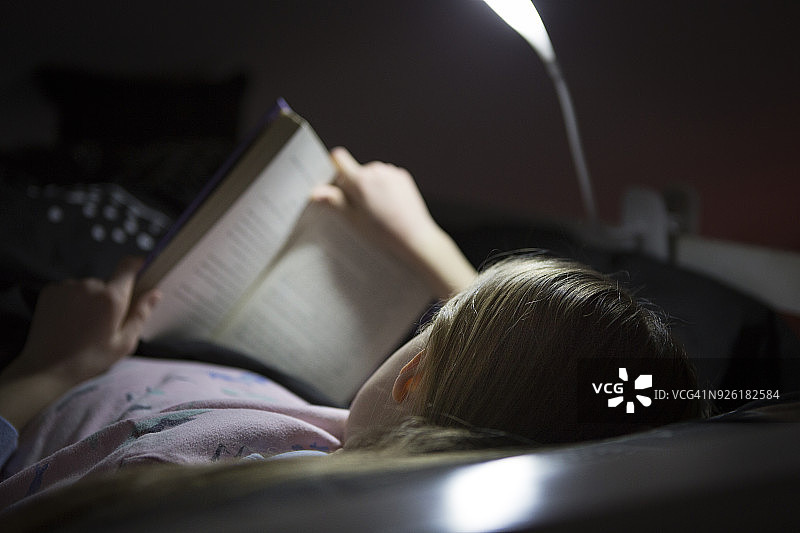 女孩(10-11)在床上看书图片素材