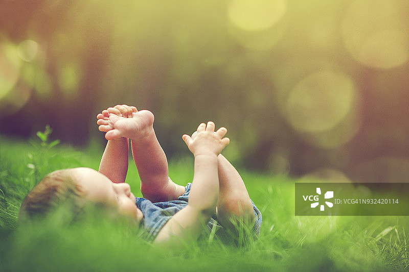 可爱的婴儿在草地上玩他的腿图片素材