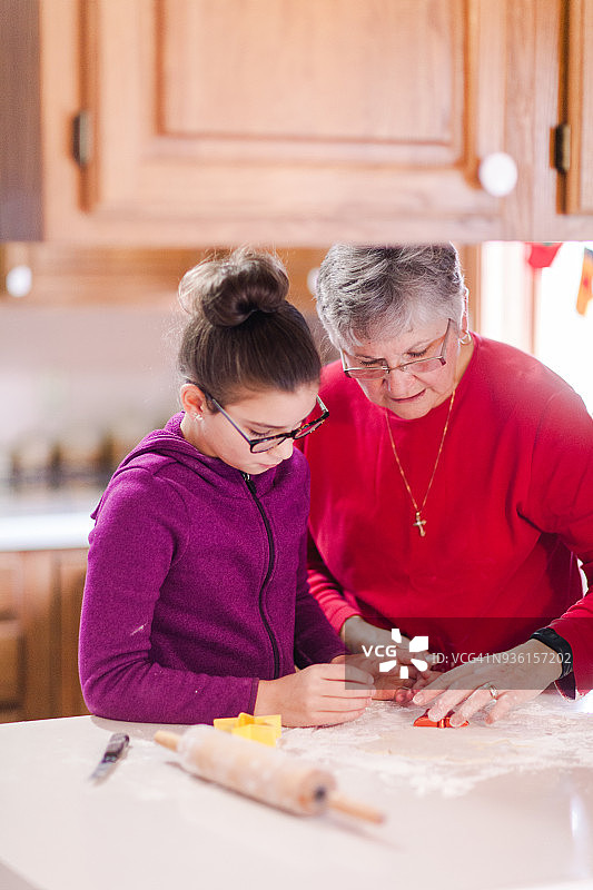 小女孩和奶奶在厨房柜台上用曲奇刀切面团图片素材