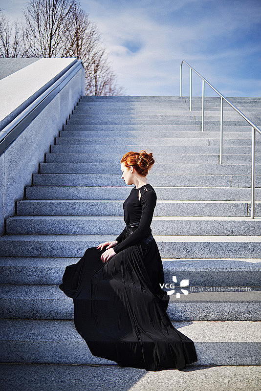 优雅的红发女子坐在台阶上，穿着黑色长袍纽约图片素材