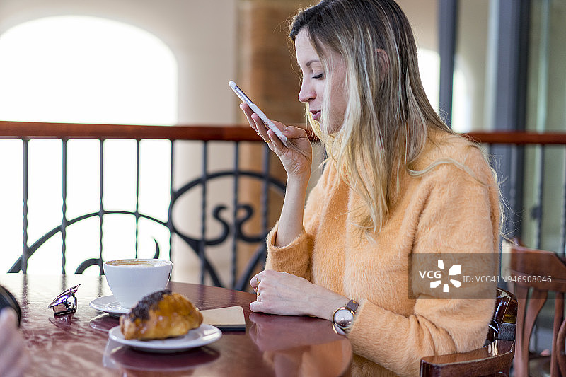 微笑的年轻女子在咖啡馆使用手机图片素材