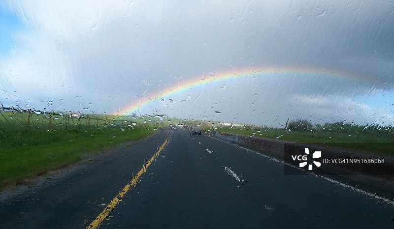 彩虹追逐。透过湿漉漉的汽车挡风玻璃看到的道路上的彩虹图片素材