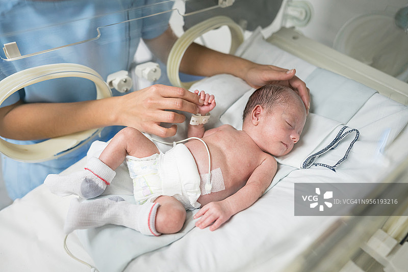 一个陌生的护士在婴儿保育箱里爱抚熟睡的新生儿图片素材