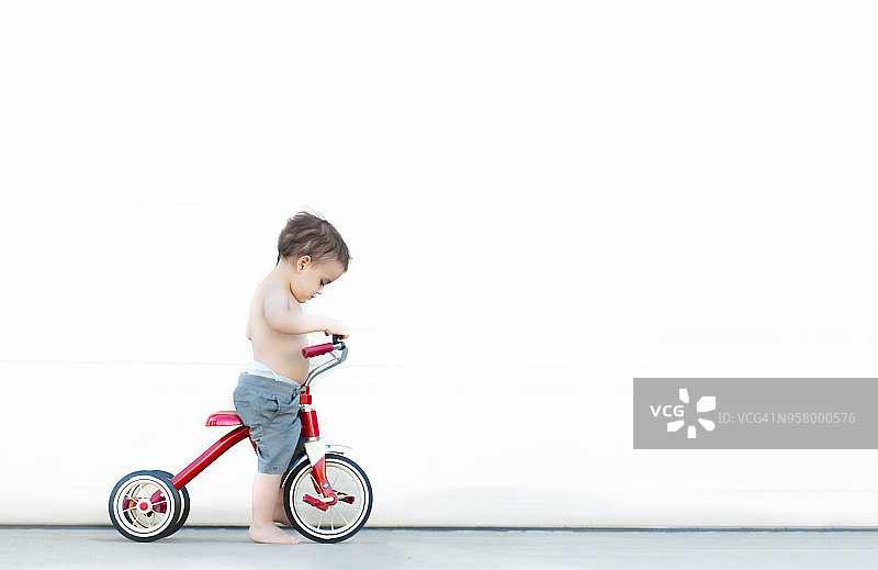 孩子站在老式的红色三轮车/自行车，而赤脚在夏天图片素材