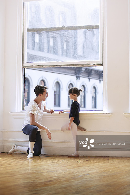 在演播室的窗户旁，男芭蕾舞老师和女芭蕾舞演员谈话的侧影图片素材
