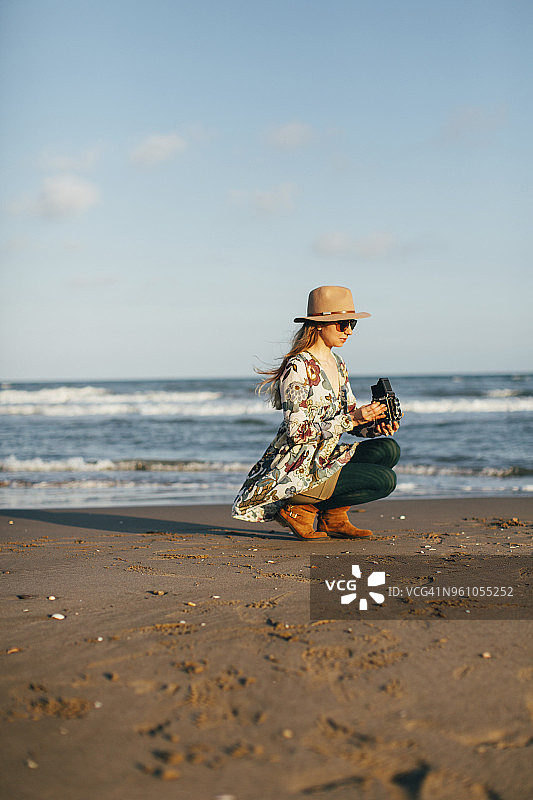 在阳光明媚的日子里，一名女子抱着照相机蹲在沙滩上图片素材