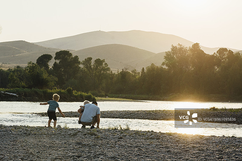背影父亲与儿子玩在湖滨对晴朗的天空在日落图片素材