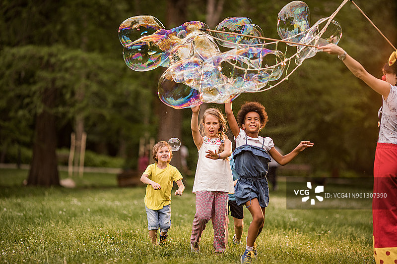 快乐的孩子们在公园里玩彩虹泡泡。图片素材