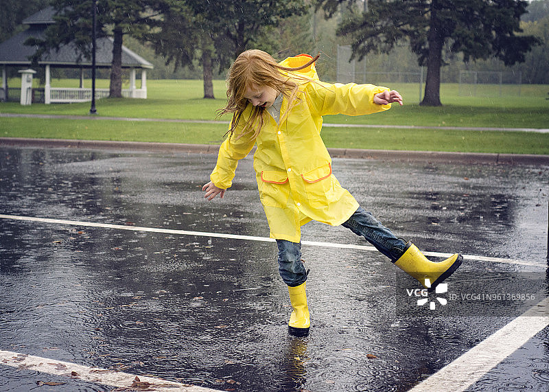 顽皮的女孩穿着雨衣在下雨的路上跳舞图片素材