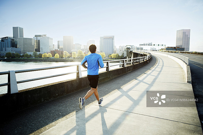 在晴朗的天空下，男运动员在桥上跑步的后视图图片素材