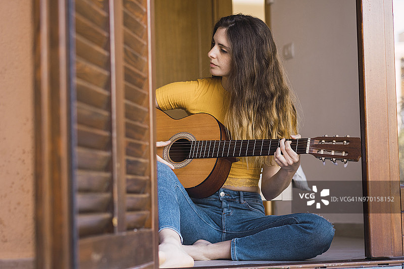 一个年轻女子坐在家里的地板上弹吉他图片素材
