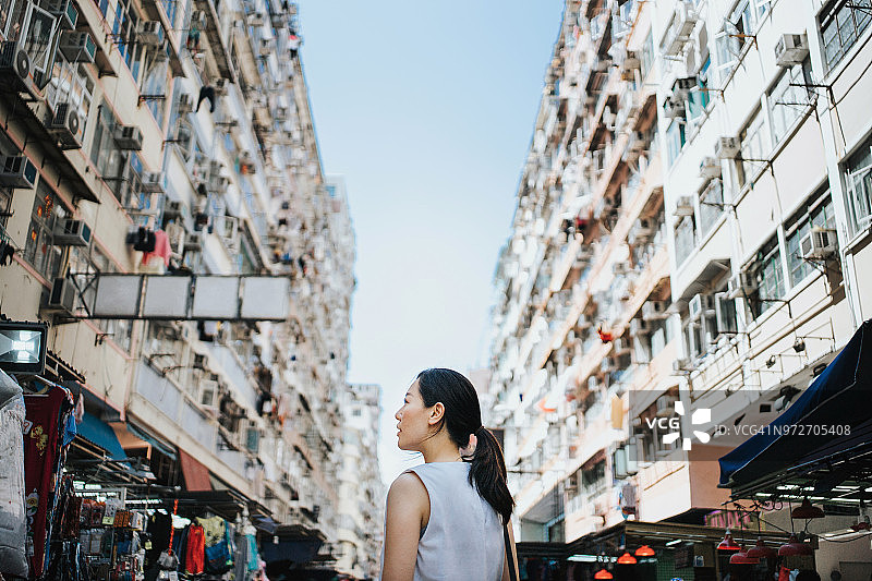 美丽的年轻女子走在香港的城市市场上，仰望天空图片素材