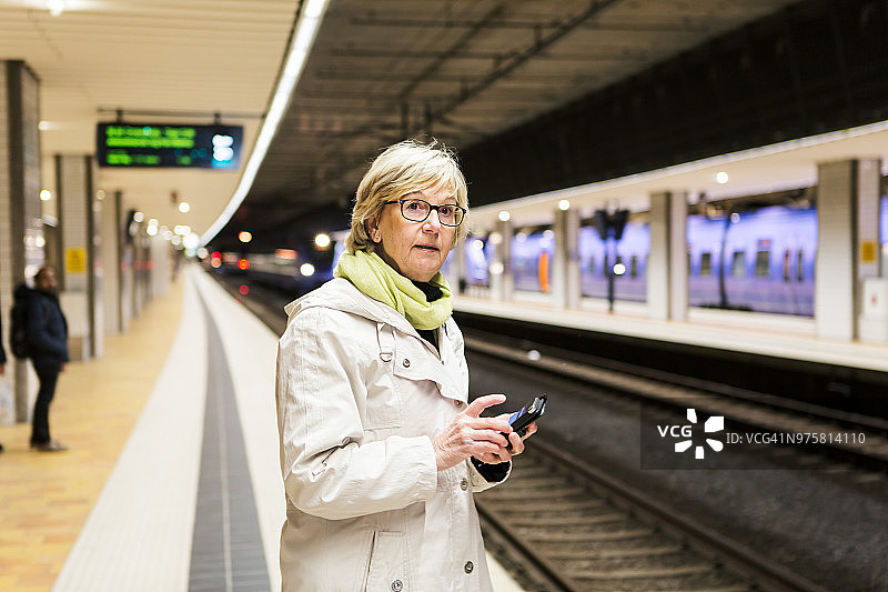 站在地铁站拿着智能手机看向别处的老妇人图片素材