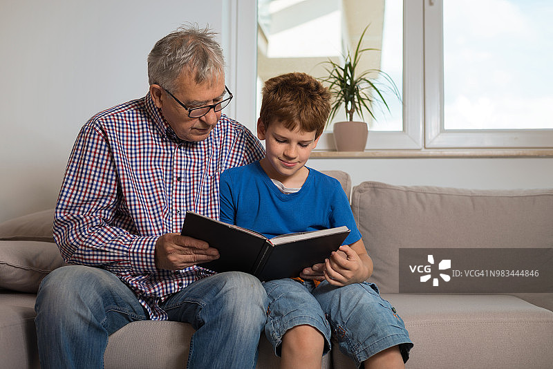 快乐的小男孩和他的爷爷一起看书图片素材