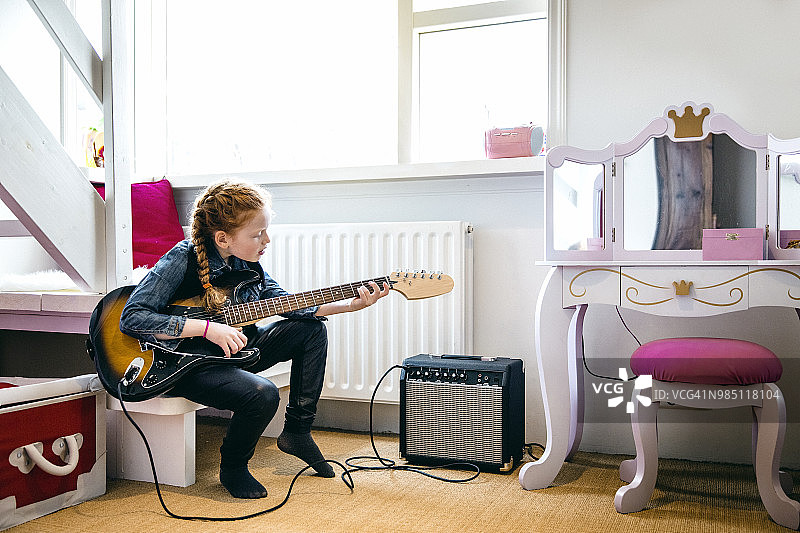 红发女孩在卧室里弹电吉他。图片素材