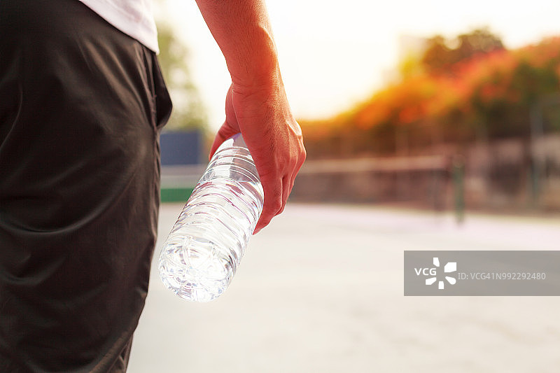 精疲力竭的男子在日落的背景下，在运动后拿着干净的饮水瓶图片素材