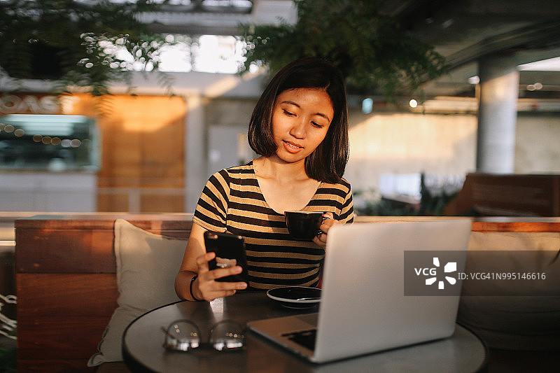 年轻的亚洲自由职业者一边喝咖啡一边用笔记本电脑工作图片素材