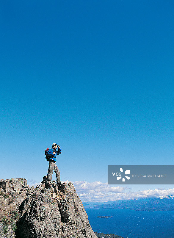 站在山顶用望远镜看风景的年轻人图片素材