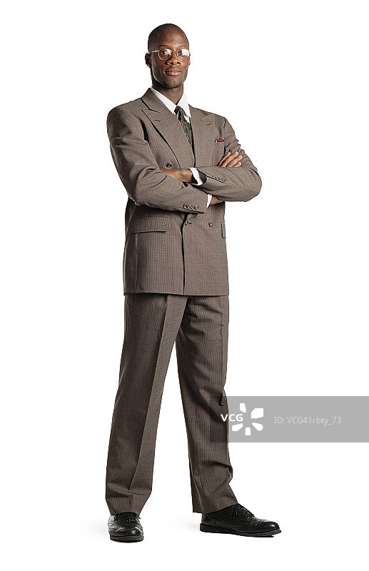 一位非裔美国男子身穿棕色西装和白色衬衫，系着领带，脚穿黑色鞋子，戴着眼镜，双臂交叉，看着镜头图片素材