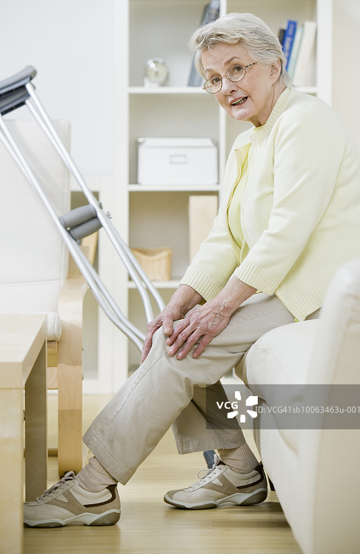 老妇人拄着拐杖坐在沙发上，抱着膝盖，画像图片素材