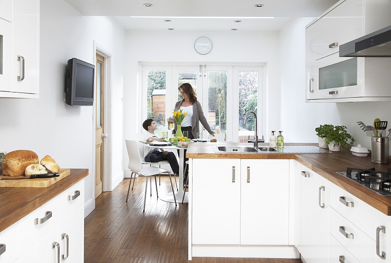 厨房餐厅配有白色的橱柜和木制的工作台面;母亲和儿子在用餐区在背景图片下载