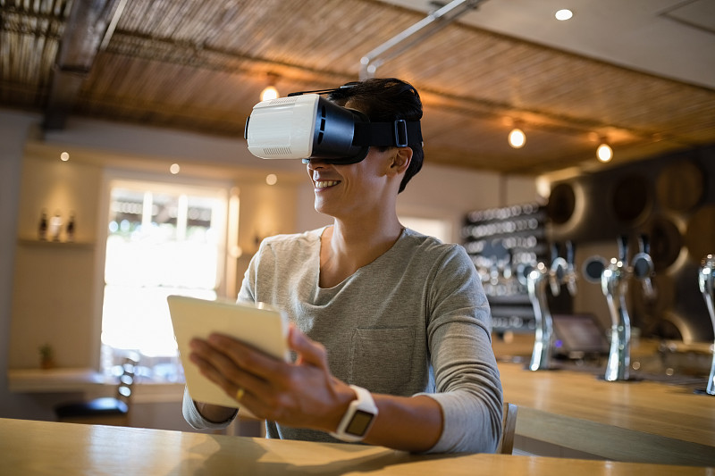 微笑的男人使用虚拟现实耳机和数字平板电脑在餐厅图片下载