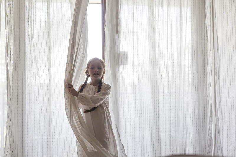 穿着睡衣的女孩站在挂着窗帘的窗户旁图片下载