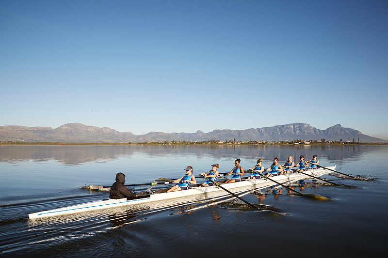 蓝天下，女桨手在阳光明媚的湖面上划桨图片下载