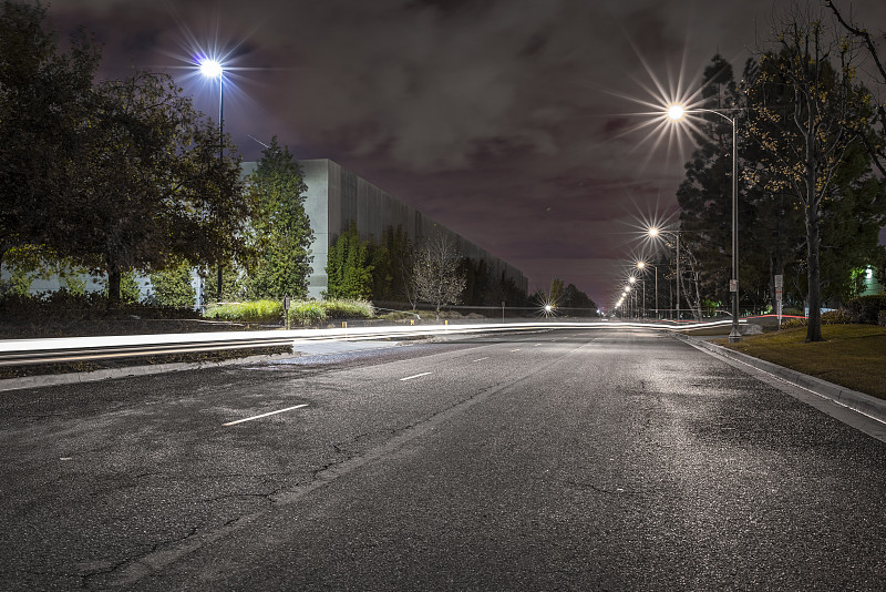 在美国圣菲斯普林斯，夜晚有路灯和现代化仓库的绿树成荫的道路图片素材