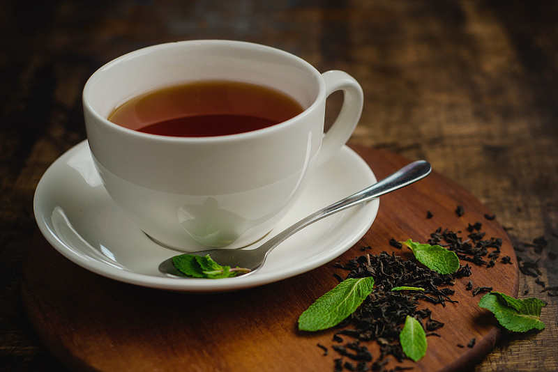 薄荷茶在白瓷杯在一个温暖的木制背景与茶冲泡和薄荷叶饮料图片素材