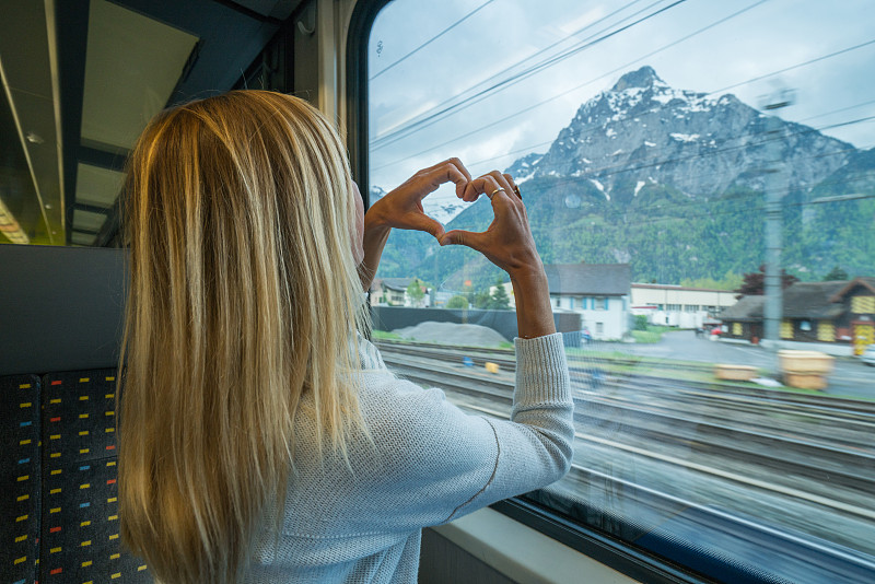 一名年轻女子在瑞士乘火车旅行，制作心形手指框架，热爱火车之旅图片下载