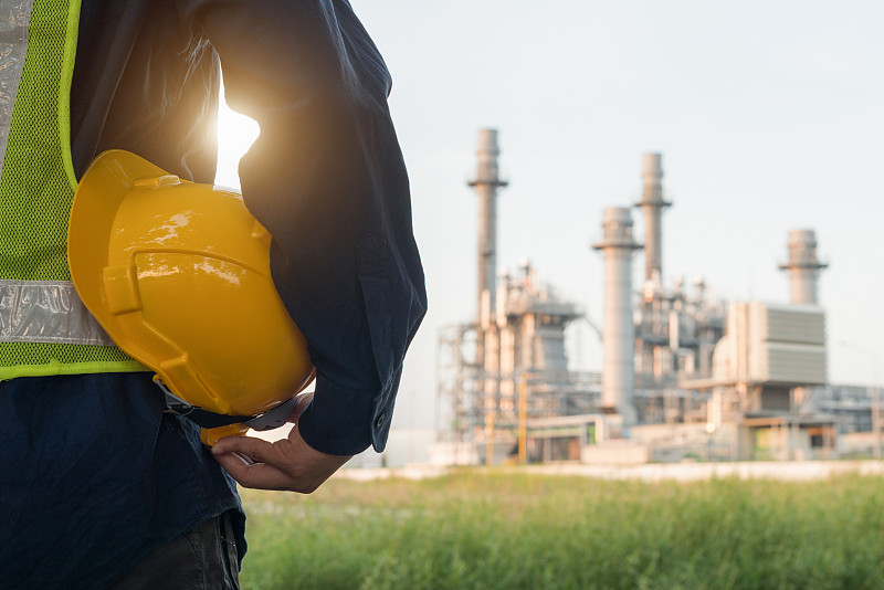 一名戴着白色安全帽的工程人员站在重石化工业炼油厂建筑结构前图片素材
