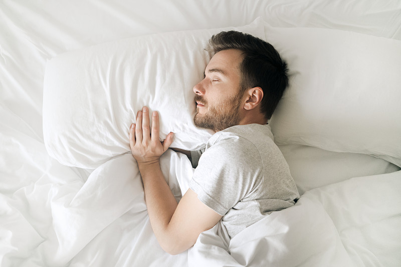 睡在白色床上的男人俯视图。放松的年轻胡子成年人在舒适的白色卧室休息图片下载