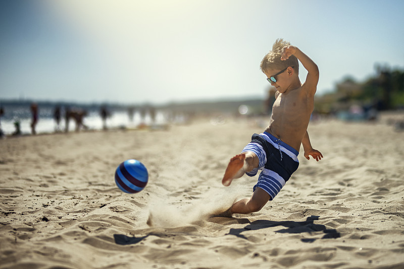 小男孩在沙滩上踢足球图片素材