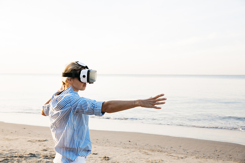 一个金发女人在泰国的海滩上用3D虚拟现实眼镜做瑜伽练习图片下载