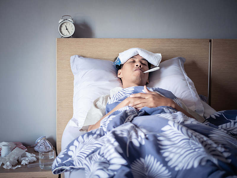 亚洲男子感冒高烧，睡在舒适的床上使用冰袋受伤减少和使用温度计测量温度。生病在家图片下载