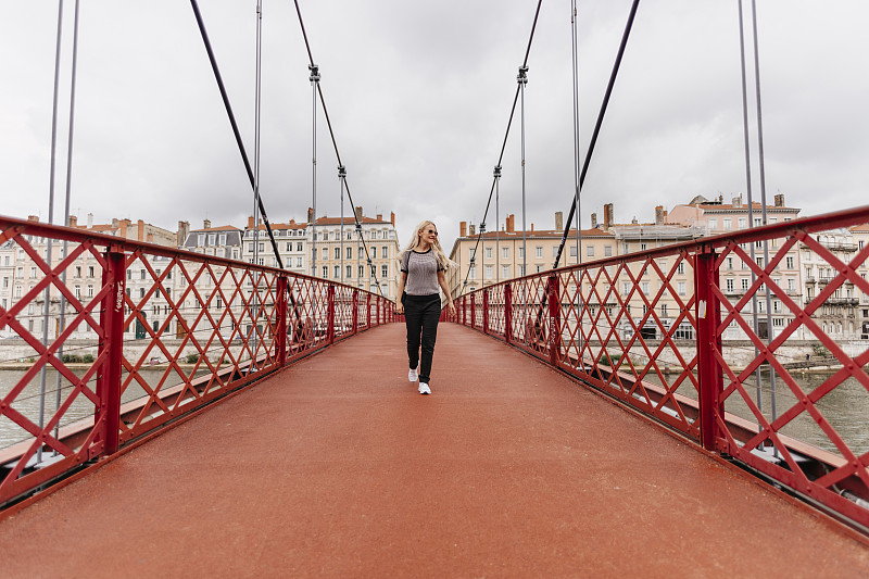 一个自信的女人走在Saone河上的Paul-Couturier人行桥上，对面是城市里的建筑物图片下载