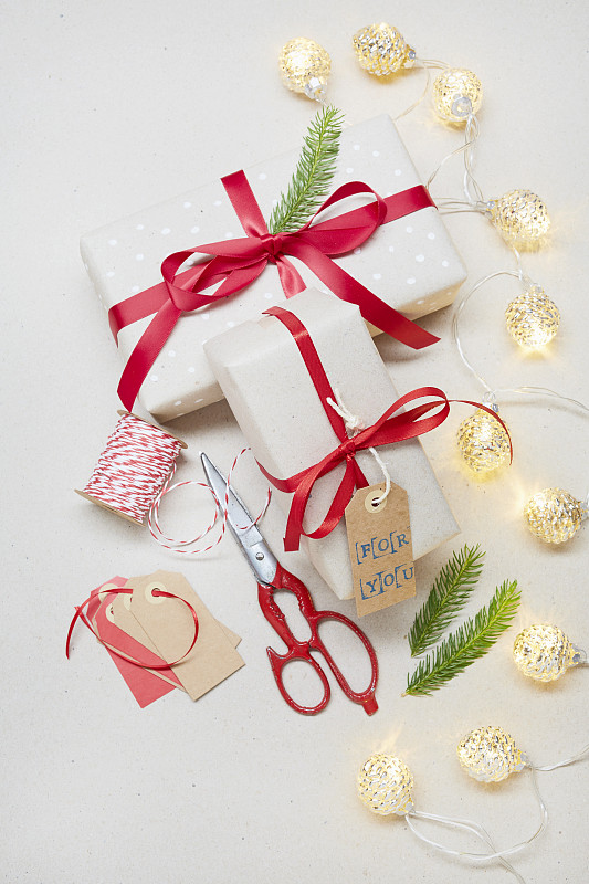 上图是在灰色背景上用“为你”的礼物标签包装圣诞礼物，红色剪刀和圣诞灯图片下载