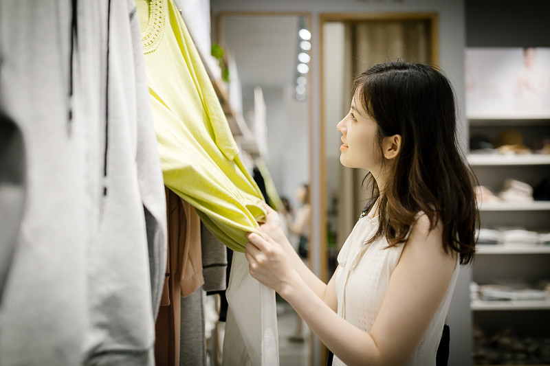 年轻的亚洲女人在服装店挑选新衣服。图片下载
