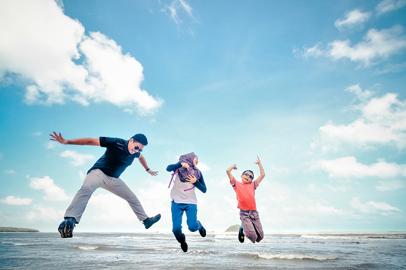 在多云的天空下，欢乐的家庭在海滩上跳跃图片素材