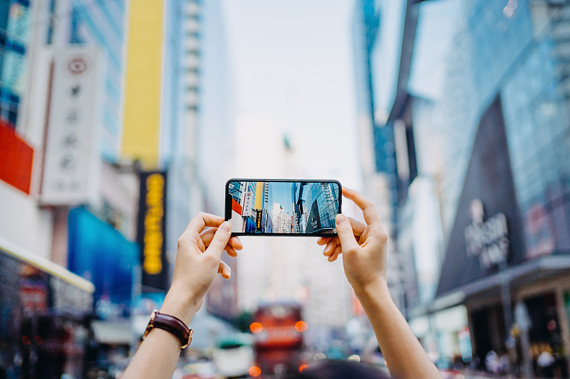 一名女性用智能手机在繁忙的市中心区与摩天大楼和城市交通拍照图片下载