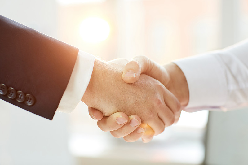 照片中的商业伙伴身着正装握手，象征着谈判成功，阳光效果摄影图片下载